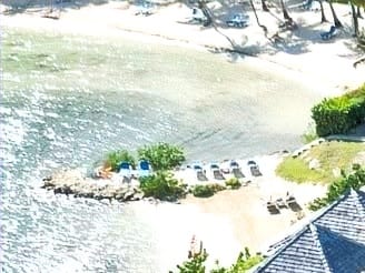 A small sandy beach with sun loungers and palm trees on the calm, clear water of the bay