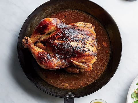A golden roast chicken in a black iron pan