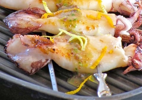 Calamari on skewers over a grill, with strips of lemon zest