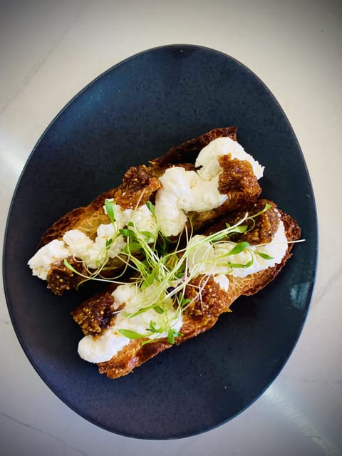 Two bruschette topped with ricotta, anchovies and micro herbs on a dark plate