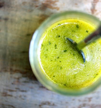 A jar of green herb dressing being stirred